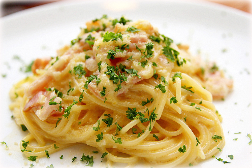 Ein Häufchen Carbonara-Nudeln auf einem weißen Teller, garniert mit Petersilie